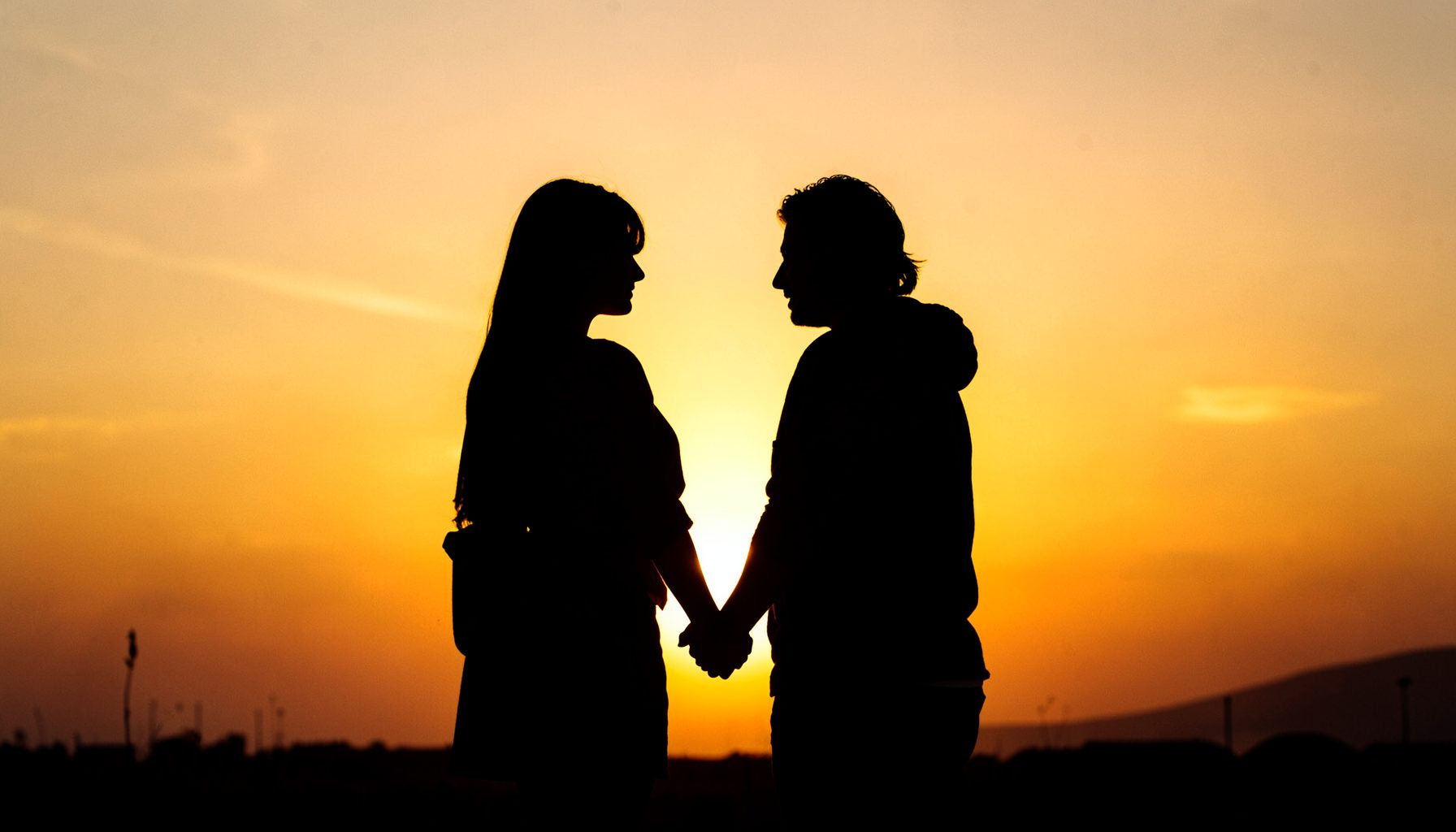 Silhouette of a couple holding hands against a golden sunset sky, warm and cinematic mood.