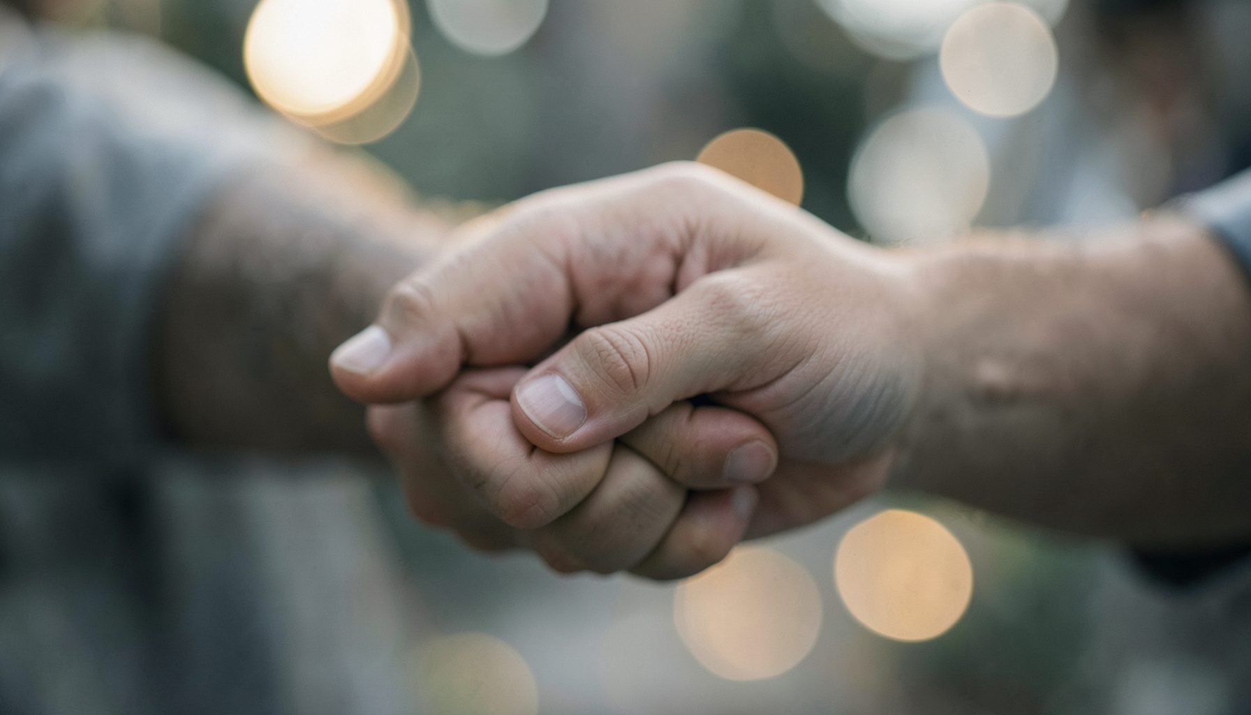 Two intertwined hands with soft bokeh lights in the background, tender and affectionate mood in muted tones.